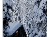 After a large winter storm has dumped two feet of snow in the lake tahoe area.A mountain cabin is surrounded by trees and everything is covered in snow.