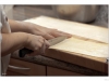 A hand is cutting pasta dough with a long knife to make linguini. A person wearing a white chef uniform is holding the knife.