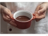 Molten chocolate ready to be baked in the oven. Two hands are holding the dish and the background is a chef coat.